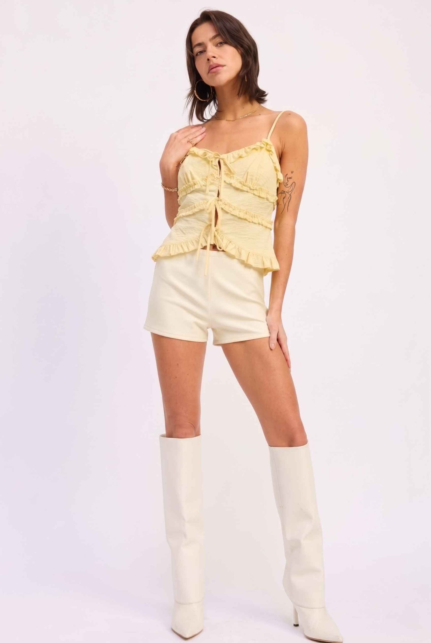 Model wearing Camille Ruffle Tie-Front Top in Yellow Tiered Sleeveless Blouse paired with micro shorts and tall heeled boots