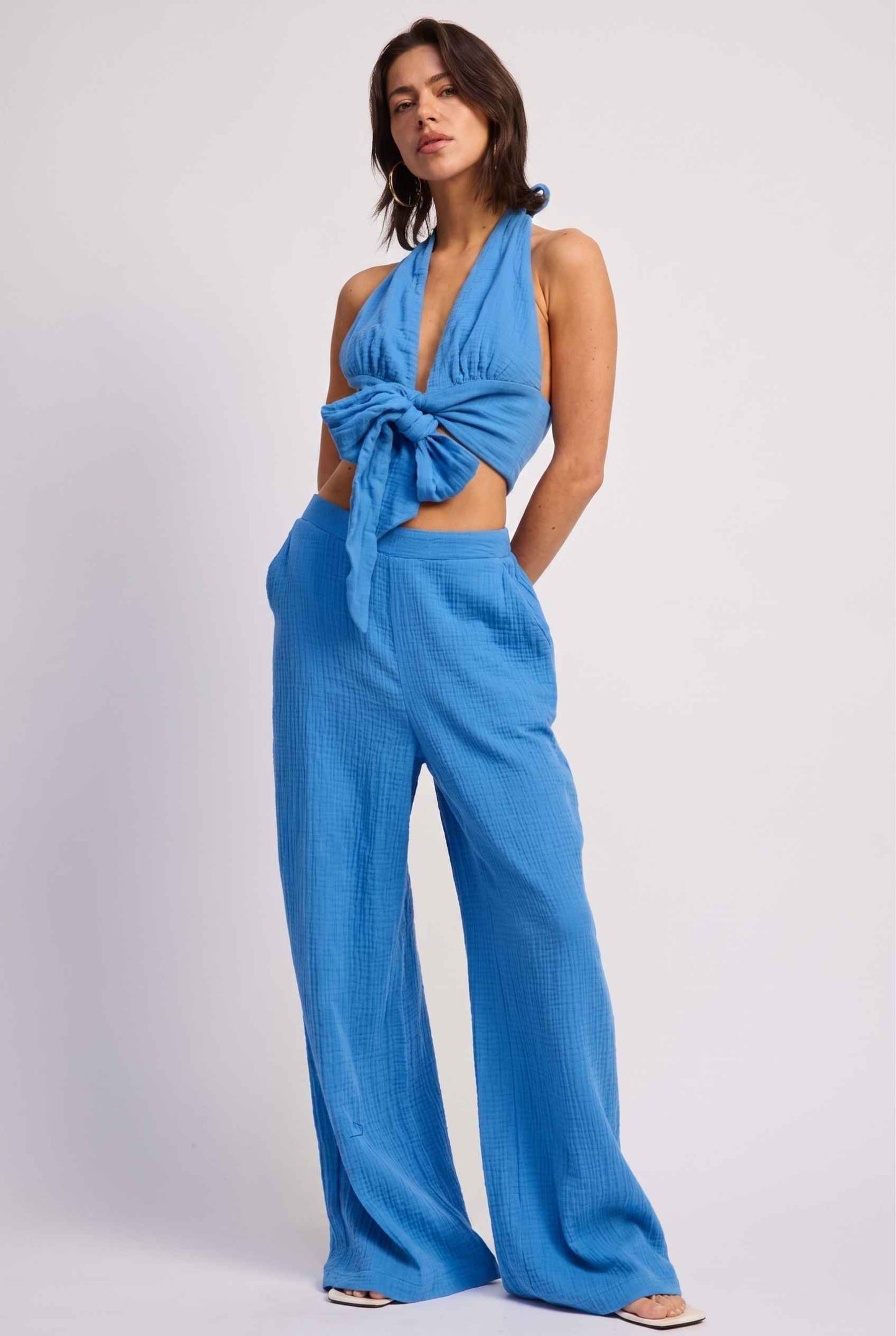 Model wearing Celine High-Waisted Gauze Pant 100% Cotton Wide-Leg Resort Pant in Blue paired with matching halter crop top and sandals