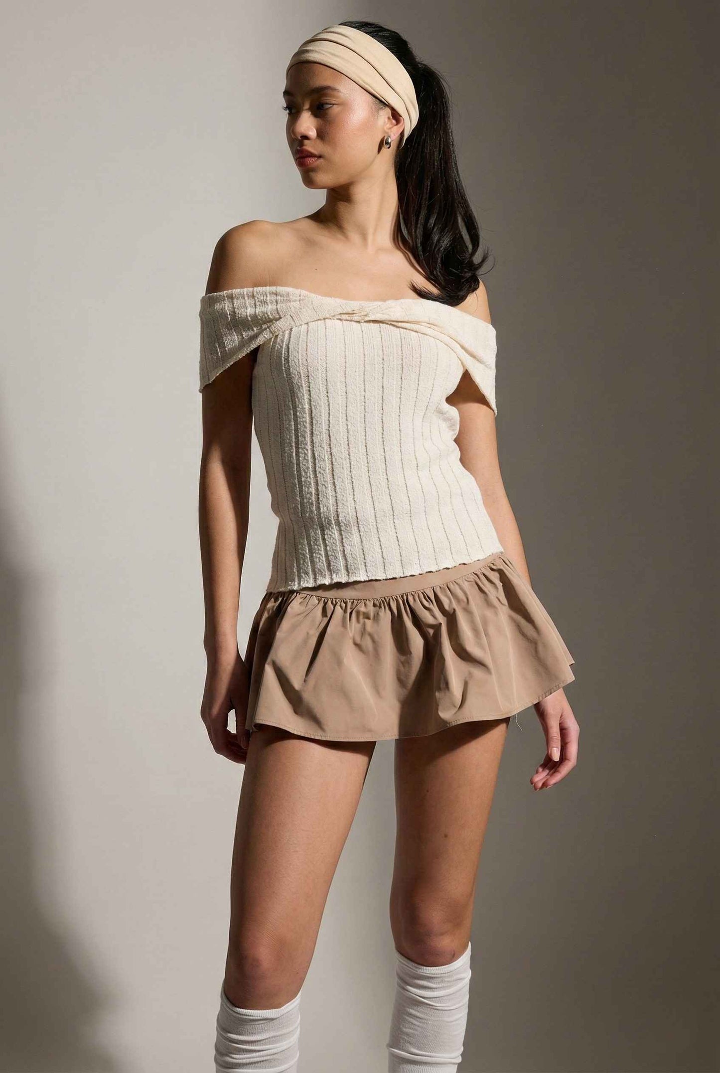 Model wearing Colette Top in Ivory Off-Shoulder Twist Front Short Sleeve Knit Top with ruffle mini skirt, knee socks against a plain background