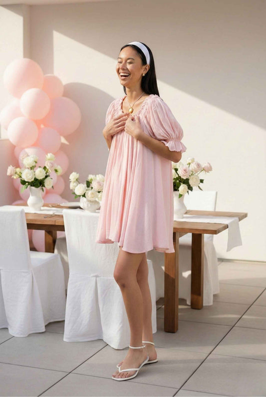 Model wearing Daphne Mini Pink Puff Sleeve Babydoll Dress laughing at celebration with balloons and flowers