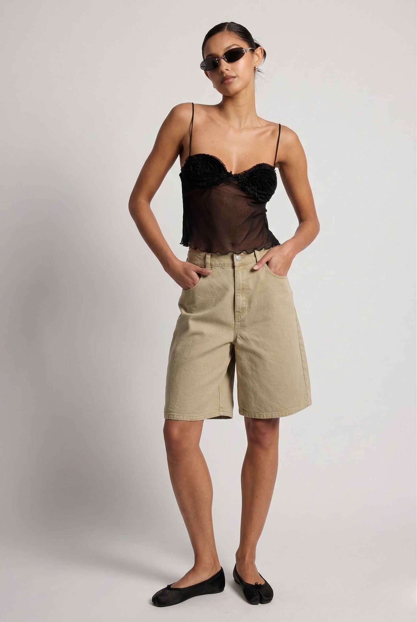 Woman wearing a Elara Top Black Sheer Mesh Camisole with 3D Floral Cups and beige shorts against a plain background