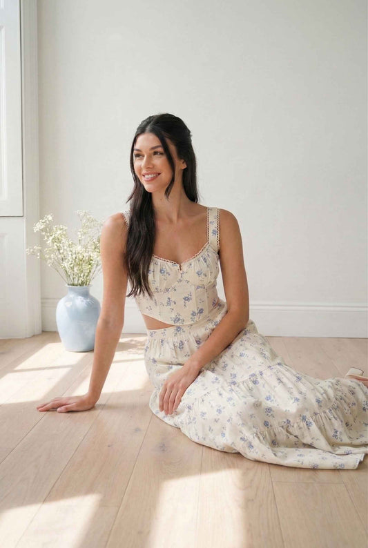 Woman in a Eliana Top White & Blue Floral Cotton Corset Crop sitting on a wooden floor with a light background