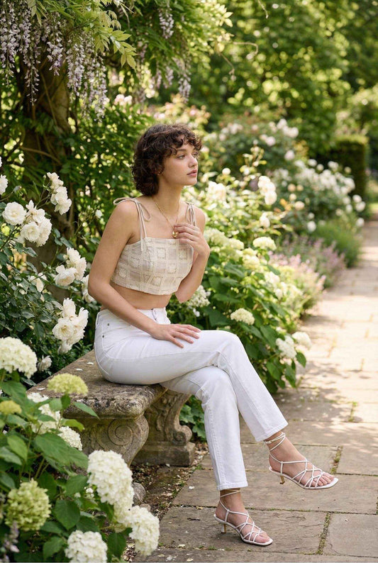Model wearing Elodie Top in Natural Jacquard Square Neck Cami with Ribbon Tie Straps with jeans and strappy sandals sitting in a luscious flower garden