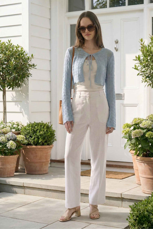 Model wearing Iris Top in Light Blue Crochet Tie-Front Shrug with Bell Sleeves with tank top, linen pants and heeled sandals standing on front porch
