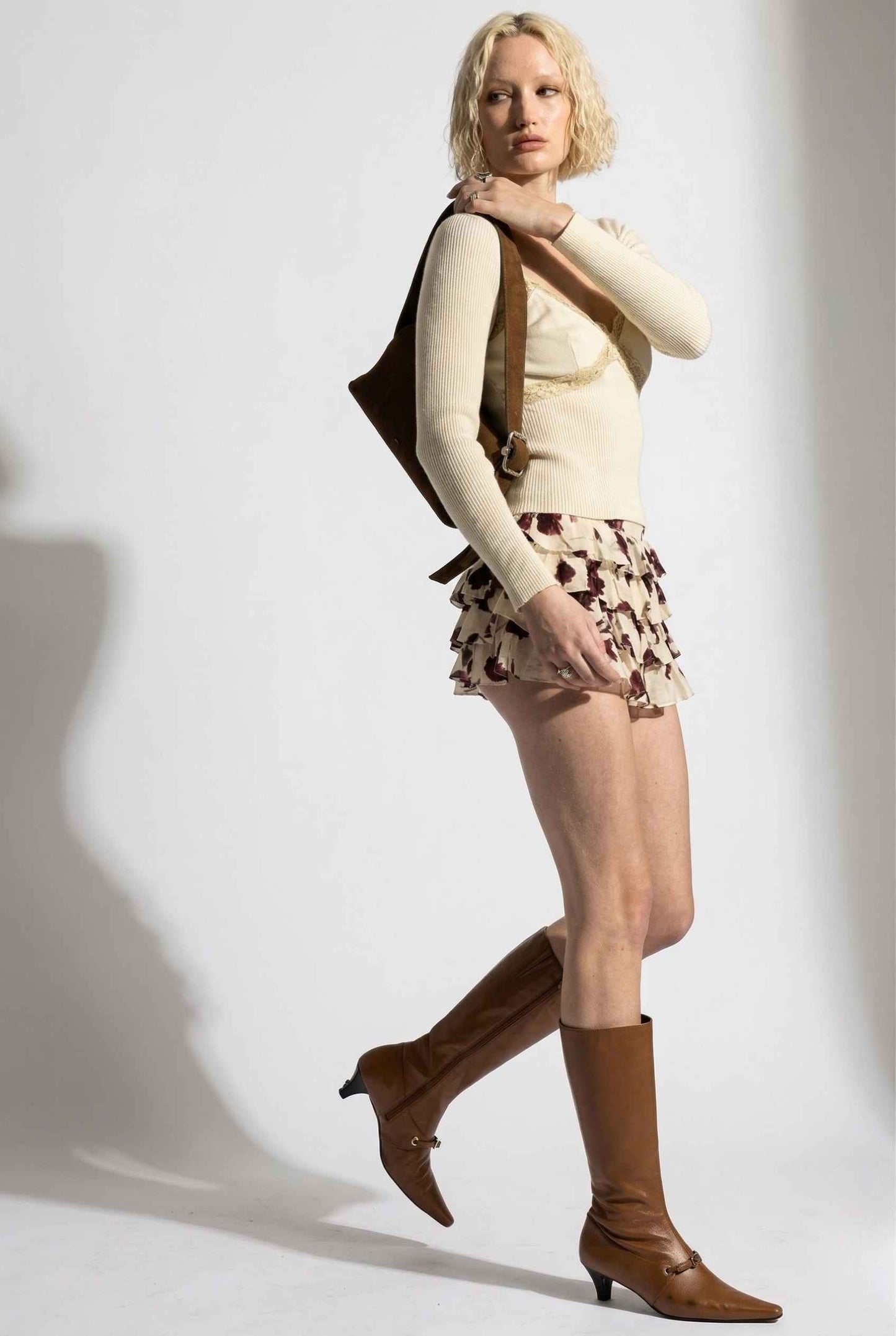 Woman in a cream sweater and Juliet Skort Cream & Burgundy Rose Floral Lyocell Ruffle Mini Skort with brown boots against a white background