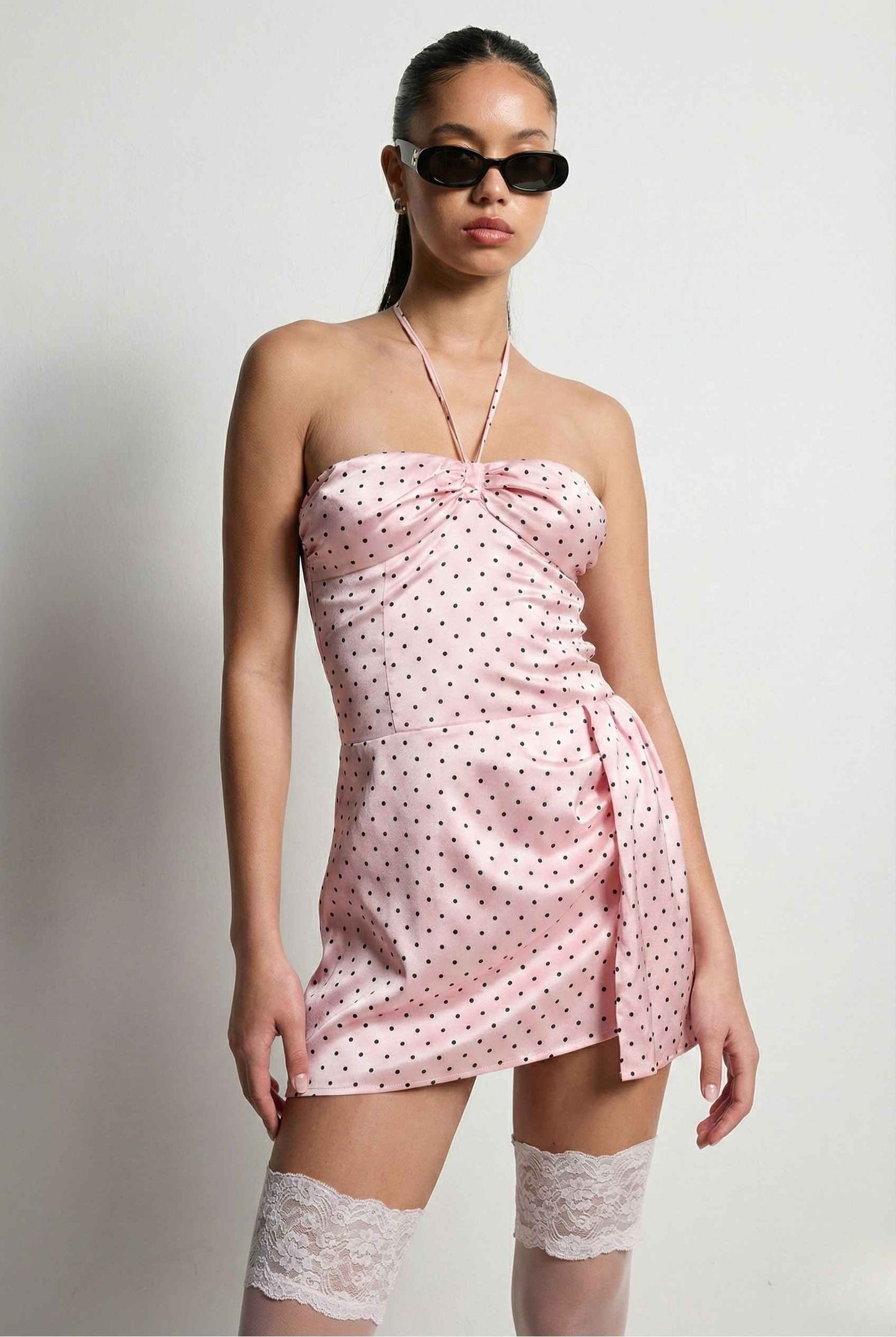 Woman wearing a Lola Mini Pink Polka Dot Satin Halter Dress with a plain background