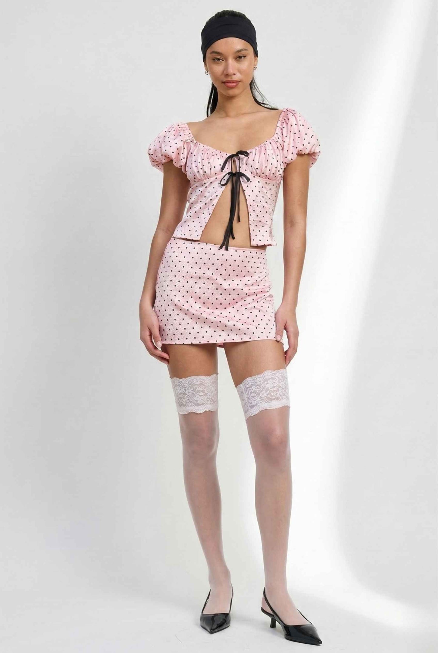 Woman wearing a Lola Top Pink & Black Polka Dot Puff Sleeve Tie-Front Blouse with a white background