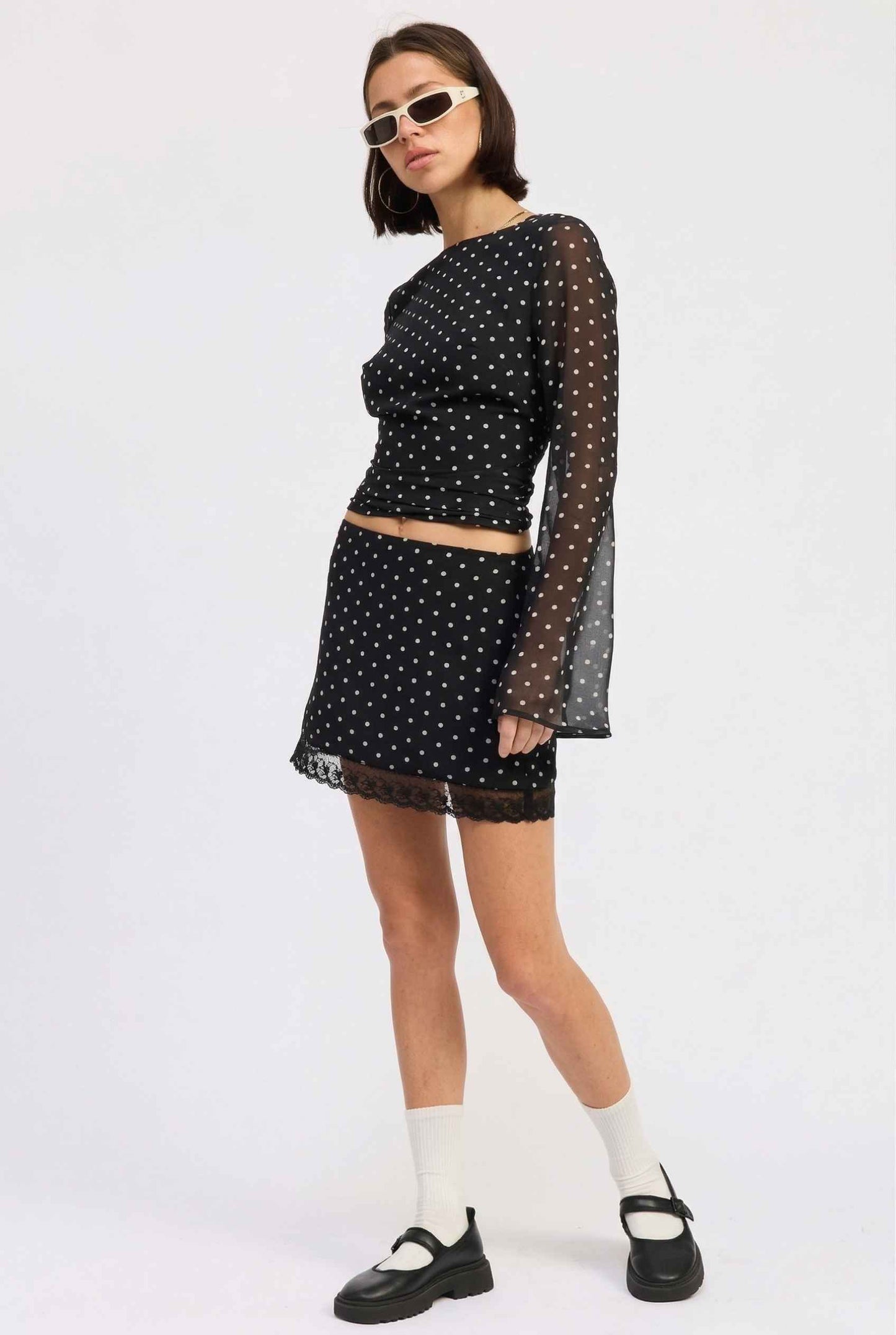 Woman wearing a Mila Skirt Black Polka Dot Mesh Mini Skirt with Lace Trim with sheer sleeves on a white background