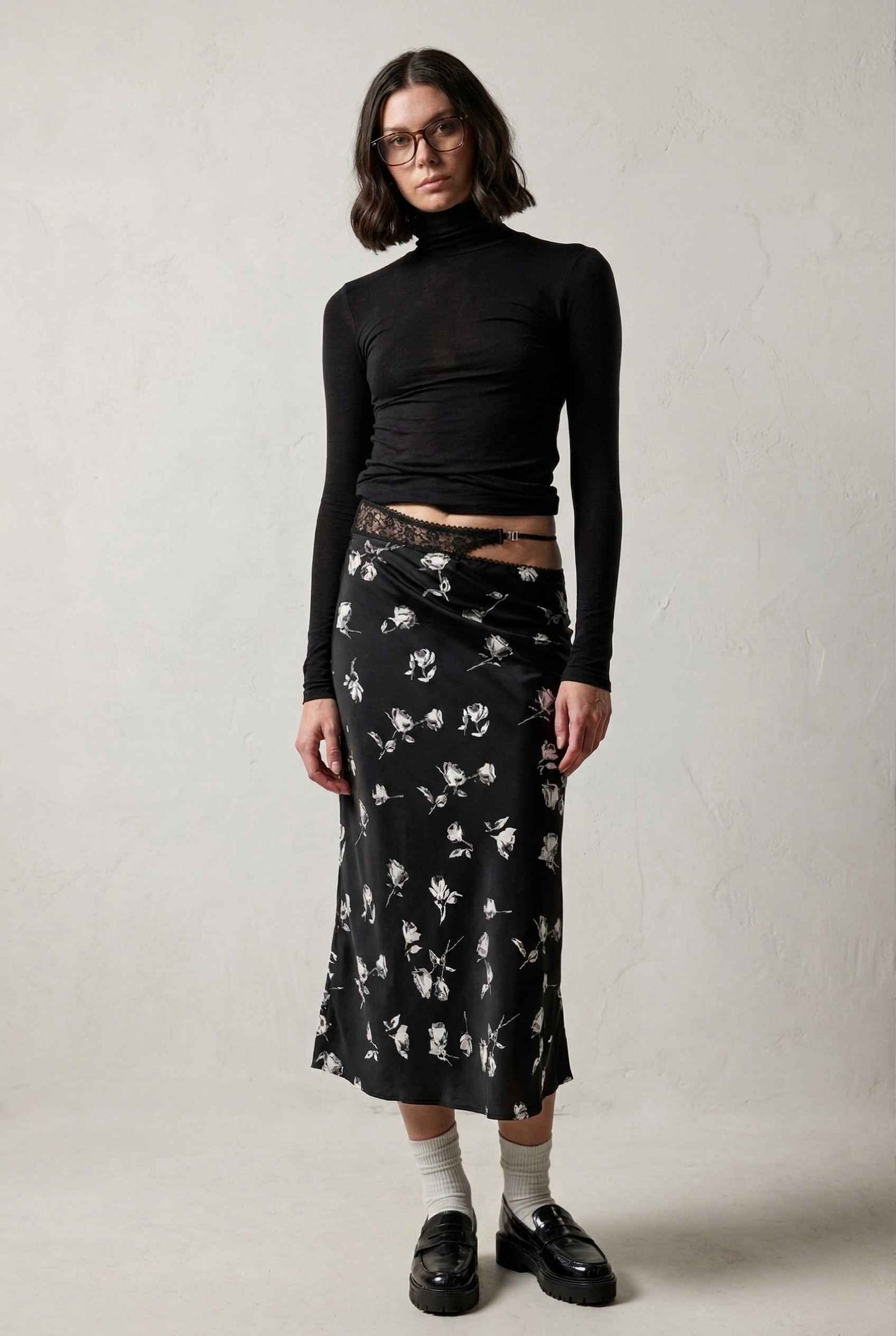 Model wearing Raven Skirt in Black Floral Satin Midi Skirt with Lace Waist paired with basic turtle neck and shiny loafers with tall socks