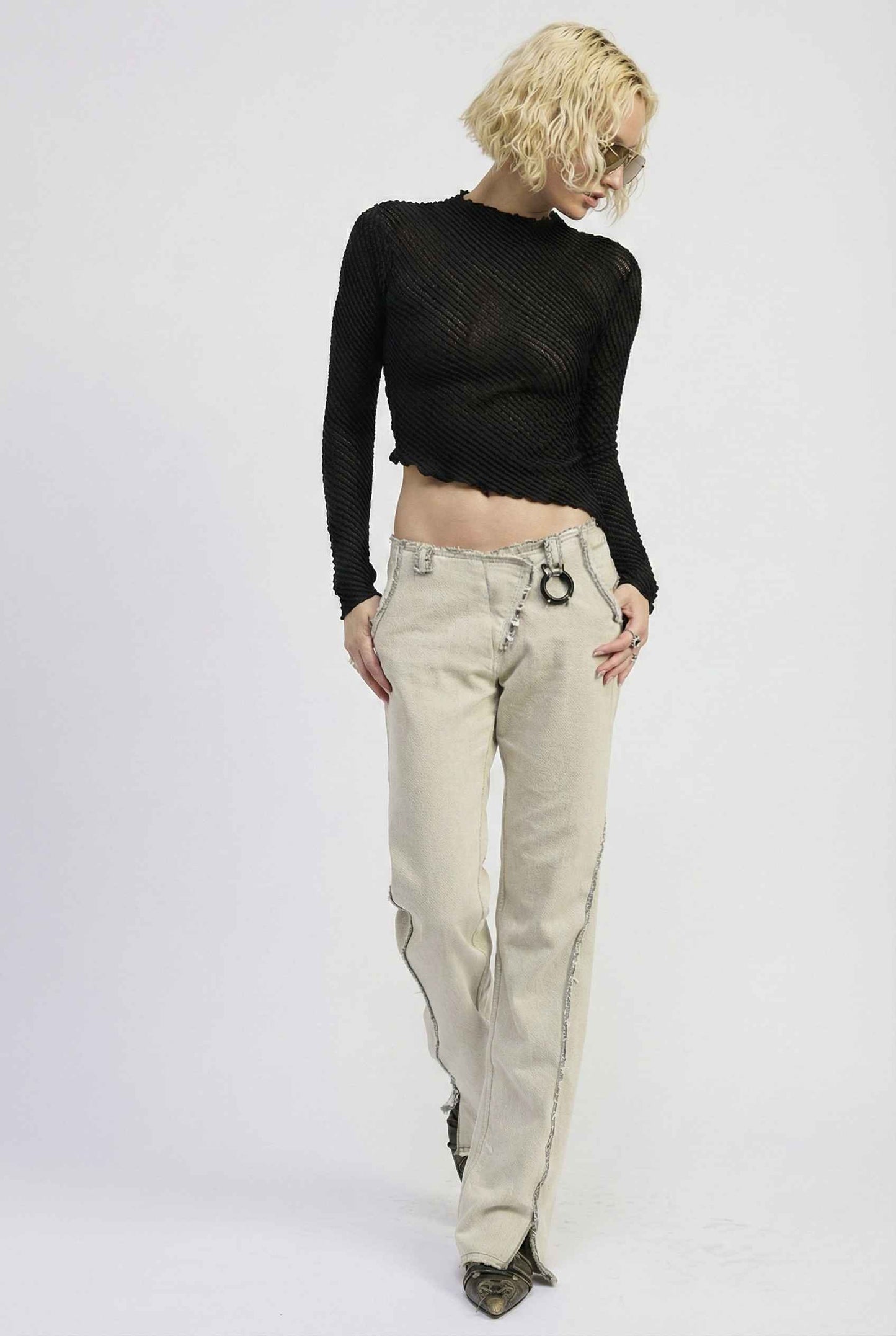Woman wearing a Ren Top Black Asymmetrical Diagonal Rib Long Sleeve and beige pants on a white background