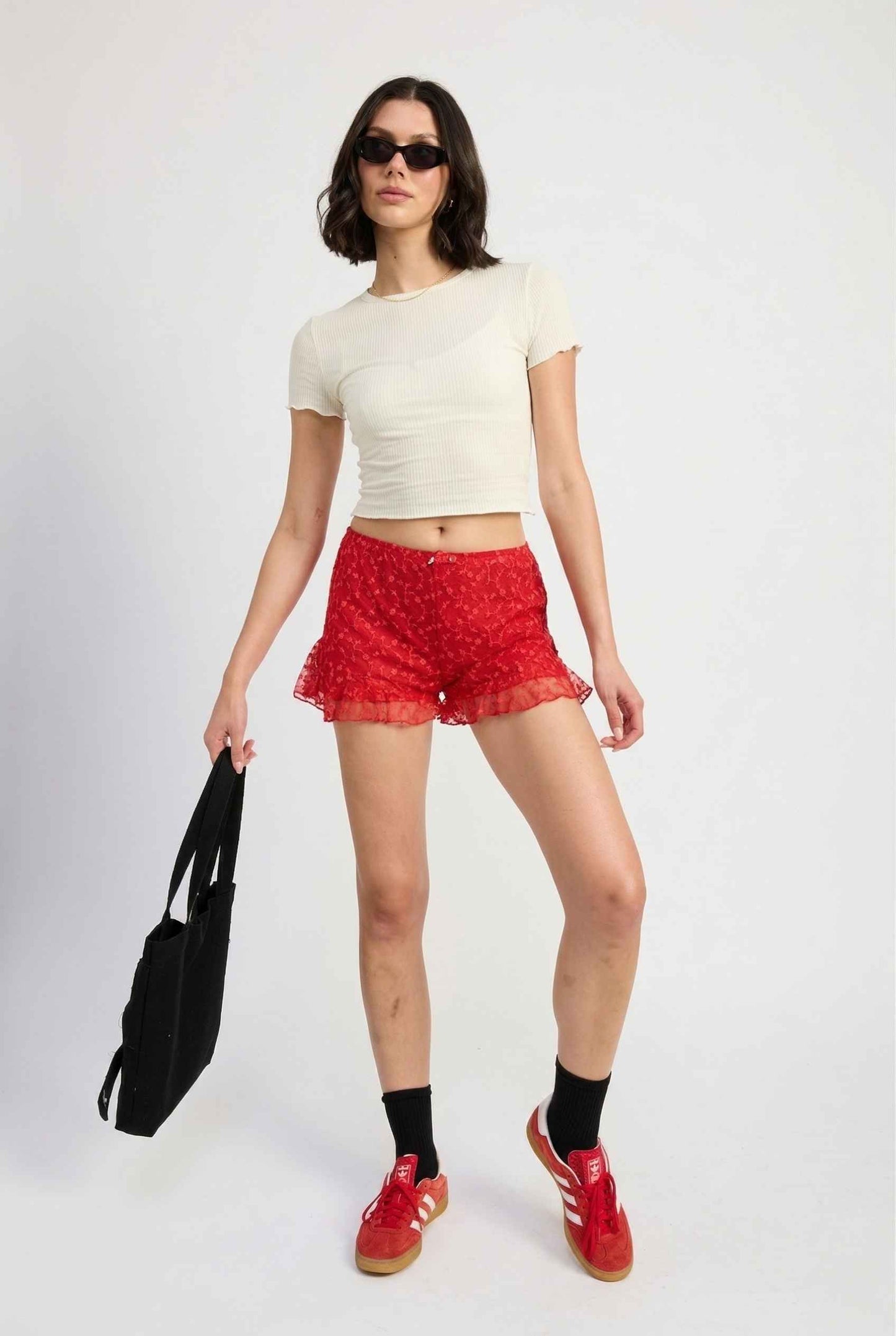 Model wearing Ruby Shorts in Red Lace Ruffle Bloomer Shorts with Bow paired with cropped t-shirt and casual sneakers with socks