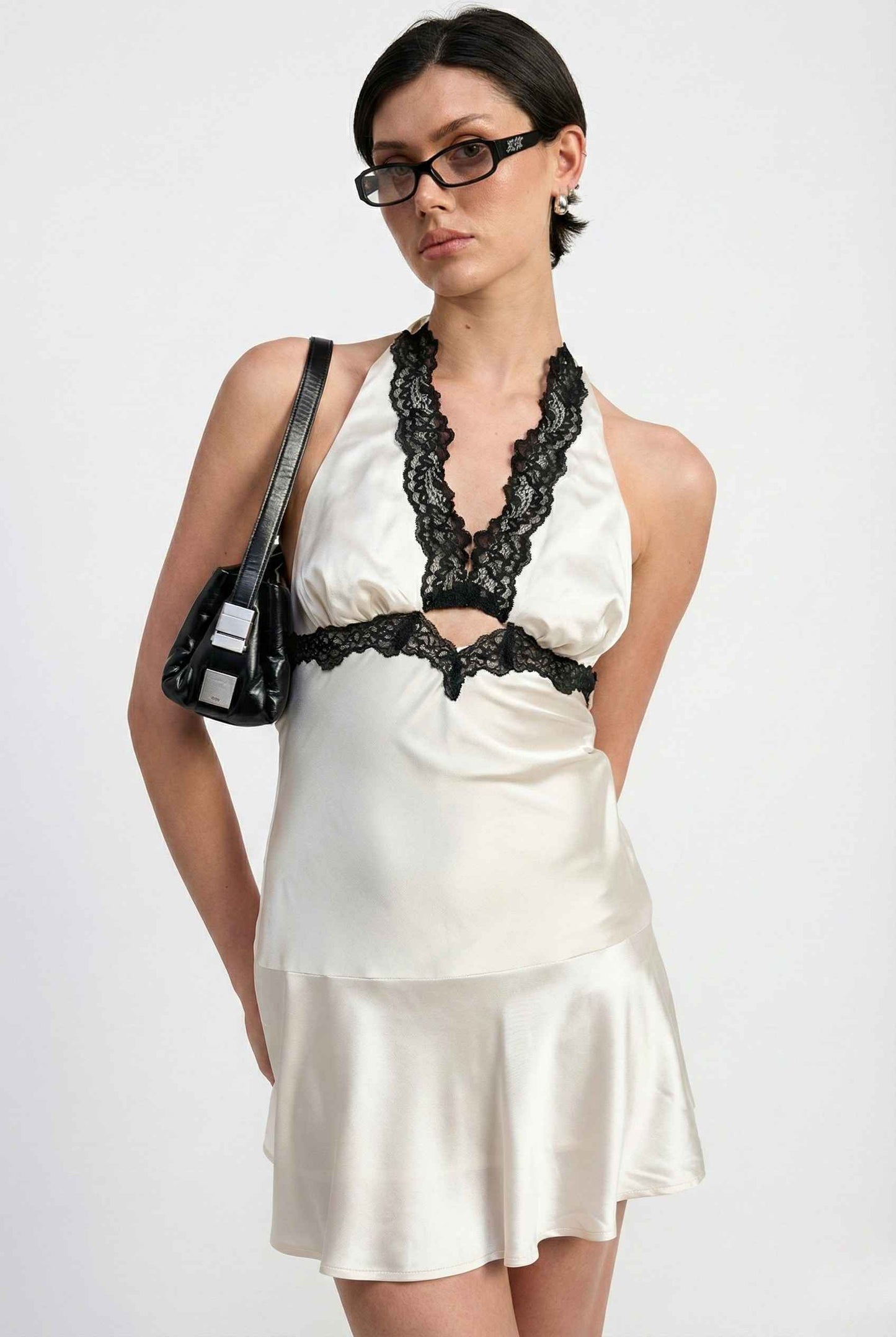 Woman wearing a Simone Mini Ivory Satin Halter Lace Trim Dress with black lace details on a white background