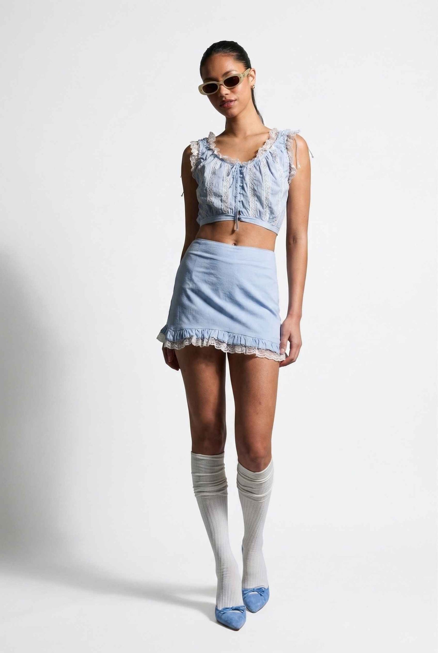 Model wearing Skye Skirt in Light Blue Cotton Mini Skirt with Delicate Lace Trim paired with matching top and heels with knee stockings