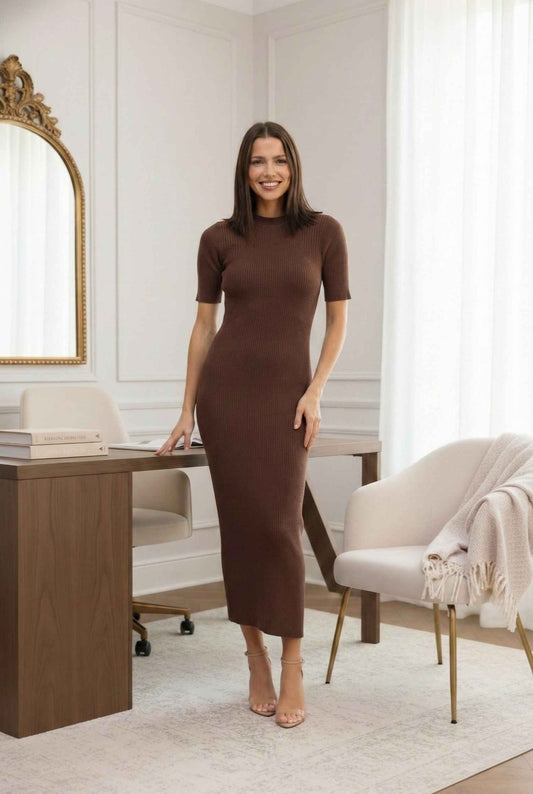 Woman in a Sloane Midi Brown Ribbed Short Sleeve Dress standing in a stylish room with a desk and chair.