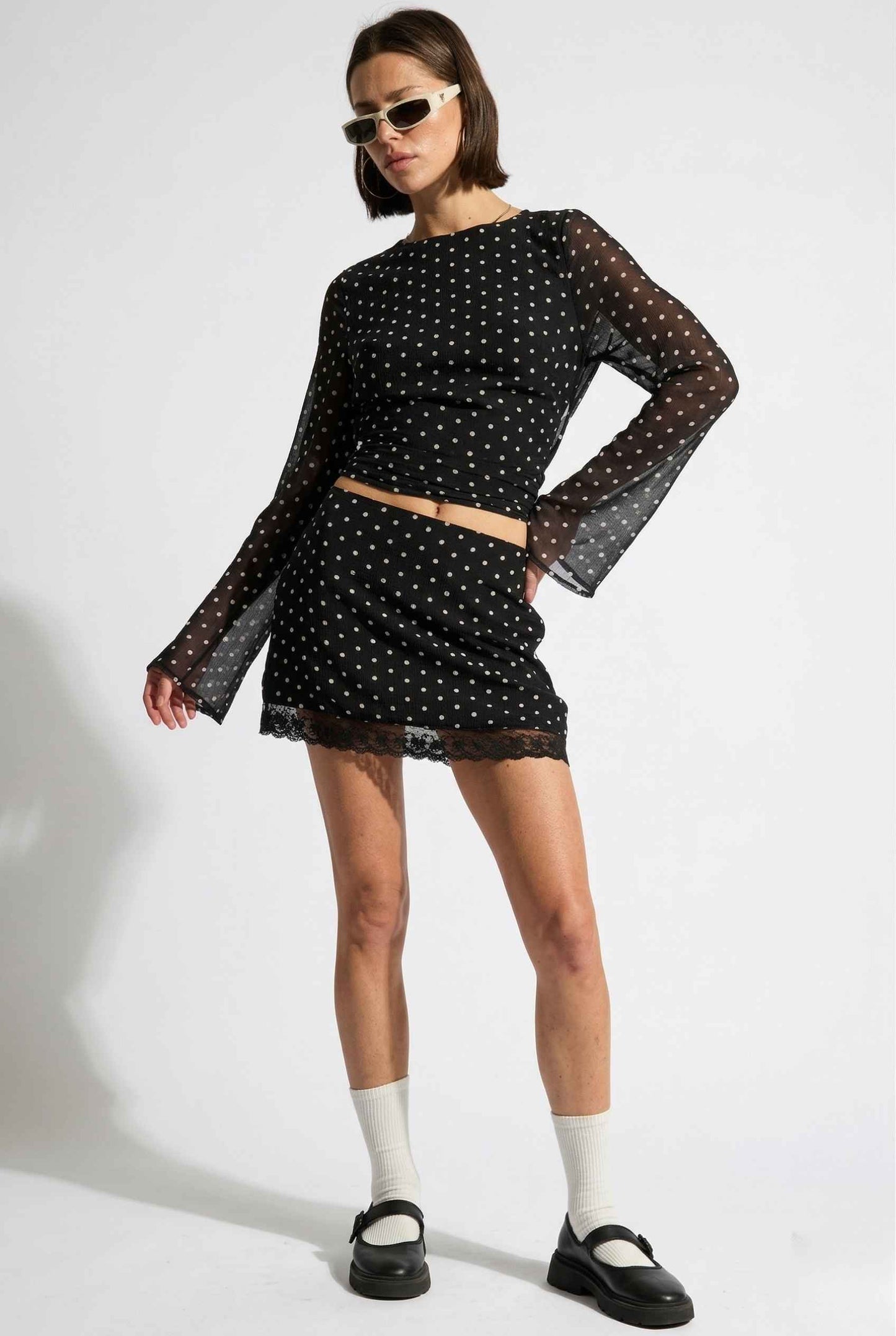 Woman wearing a Stella Top Black & White Polka Dot Sheer Long Sleeve with sheer sleeves on a white background