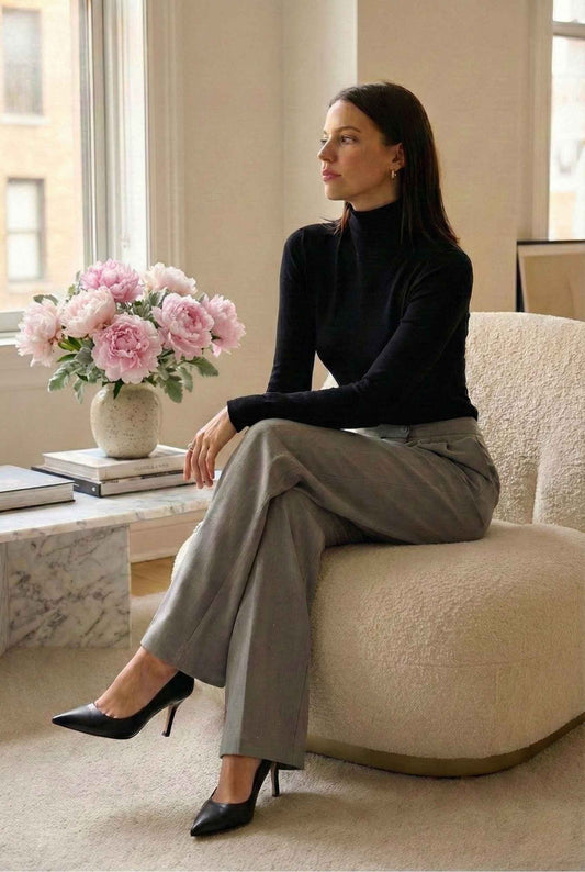 Model wearing Stella Trousers in Grey Rhinestone Embellished Pleated Wide-Leg Pants with long sleeve sweater top and pumps sitting in luxury apartment