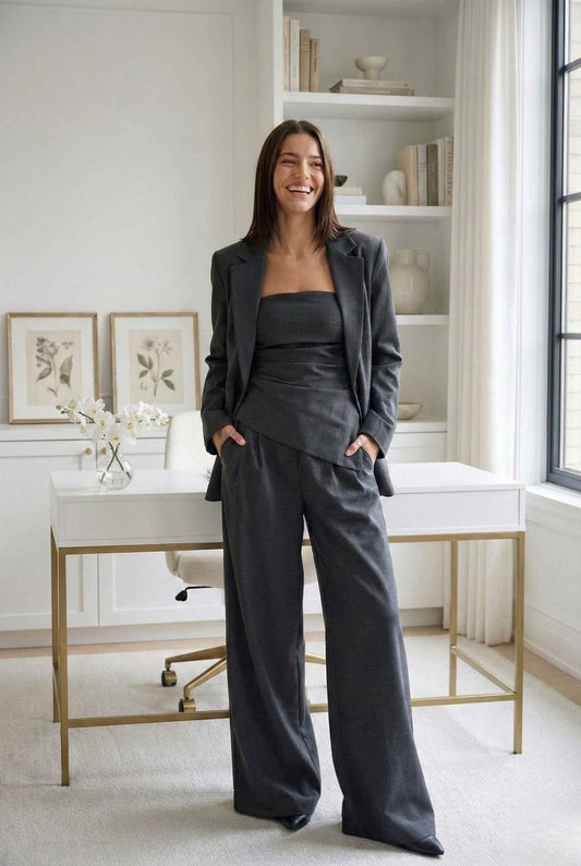 Woman in a Sutton Bustier Charcoal Grey Asymmetrical Strapless Top standing in a well-lit room with a desk and shelves.
