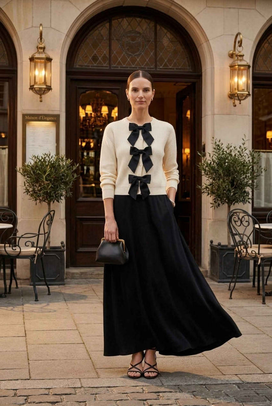 Woman wearing The Camille Bow Cardigan Ribbed Shaker Cream Knit Sweater with a flowy skirt and strappy heels standing in front of a luxury restaurant
