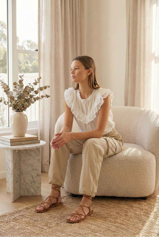 Model wearing Wren Pants 100% Nylon Parachute Cargo Pants in Taupe with ruffle blouse and strappy sandals sitting in luxury living room
