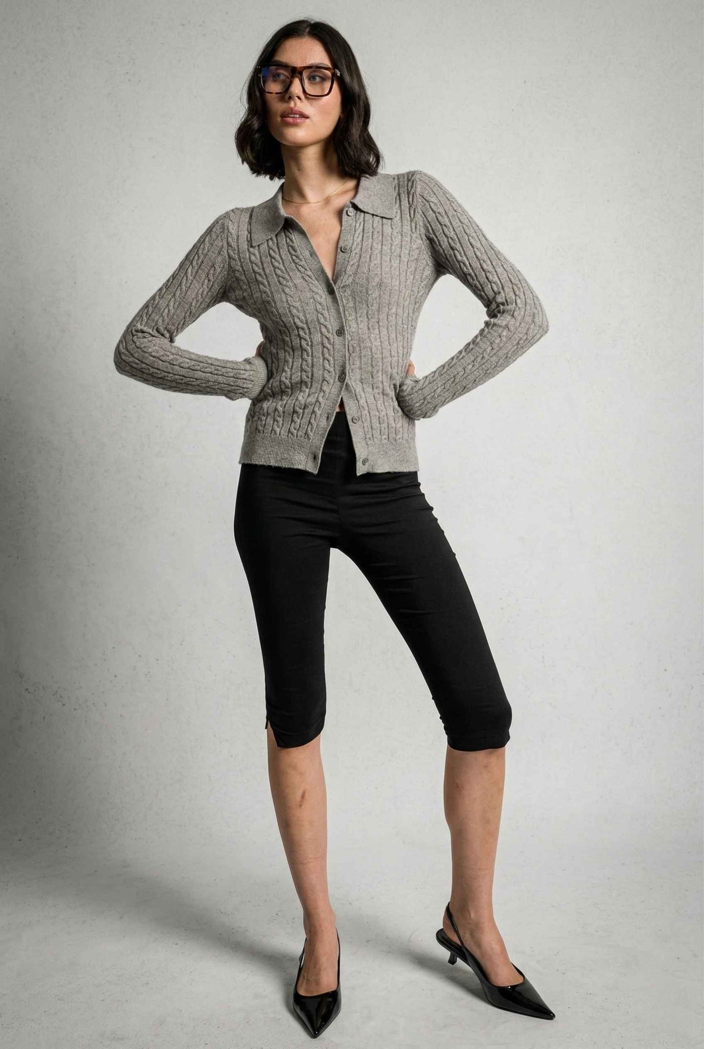 Model wearing Wren Cardigan in Grey Cable Knit Button-Up Collared Cardigan with capri pants and heels on a plain background