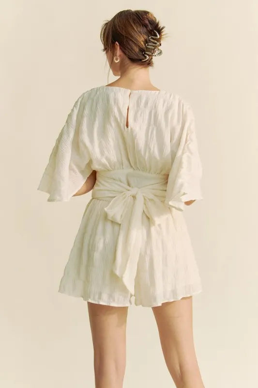 Back view of Davi & Dani Batwing Sleeve Waist Belt Romper in light fabric with a tied waist detail