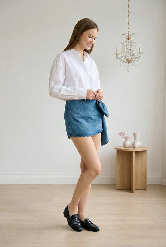 Model wearing Emory Park Denim Bow with blouse and loafers standing in feminine minimalist loft