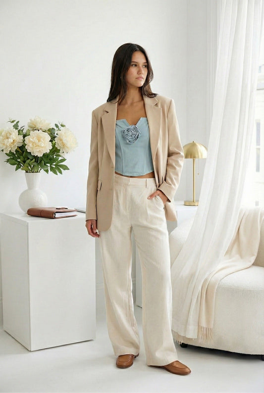 Model wearing Emory Park Light Denim Corset Top With Rosette Detail with blazer and light trousers standing in minimalist feminine apartment