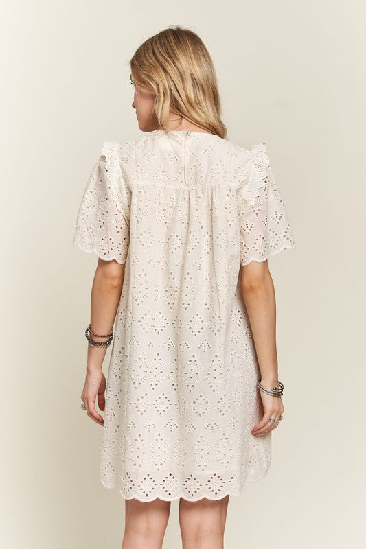 Back view of a cream ruffled eyelet dress with short sleeves and intricate eyelet details