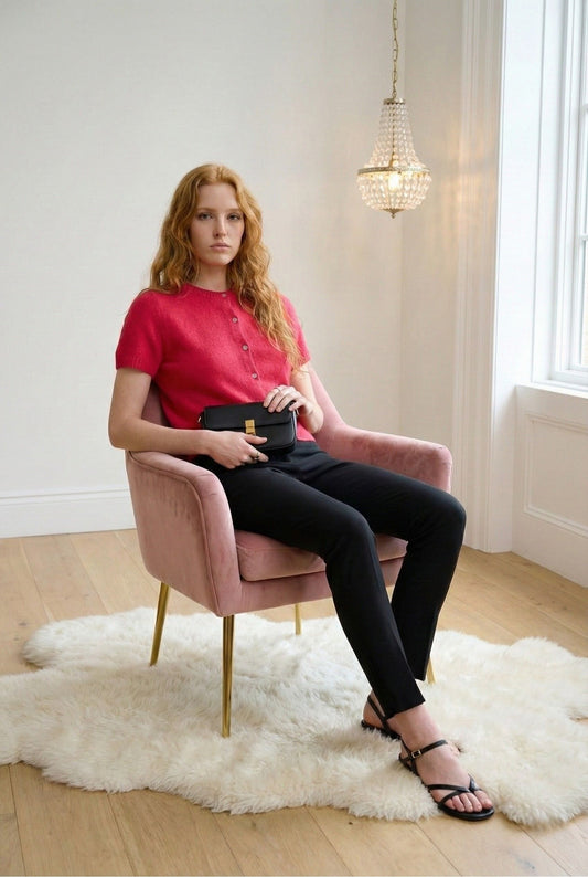 Model wearing a Red Emory Park Short Sleeve Button Up Cardigan with trousers and sandals sitting on a chair in minimalist luxury loft