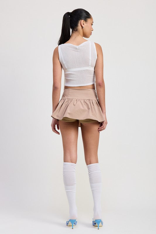 Back view of model wearing Emory Park sleeveless sheer bow top in white paired with beige skirt and white knee-high socks