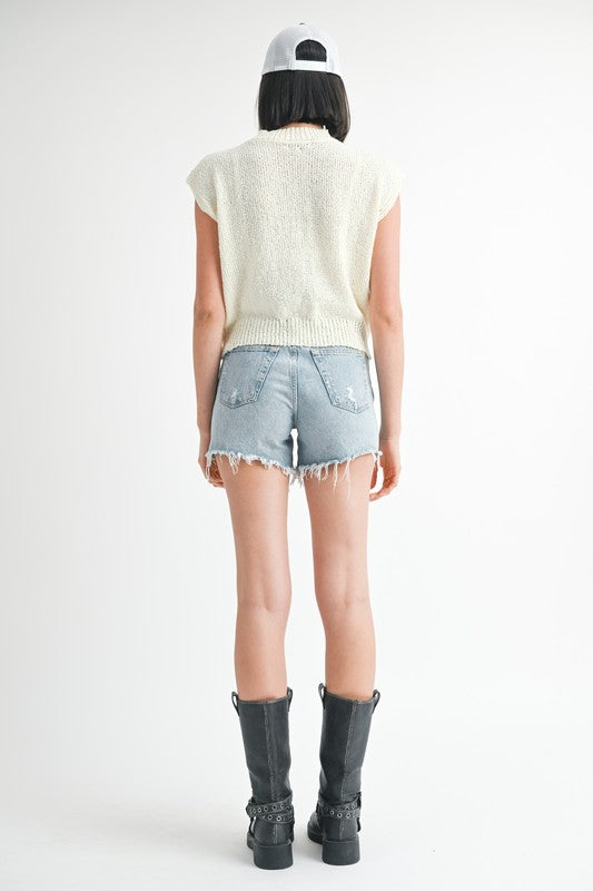 Back view of model wearing Emory Park sleeveless sweater top paired with denim shorts and black boots