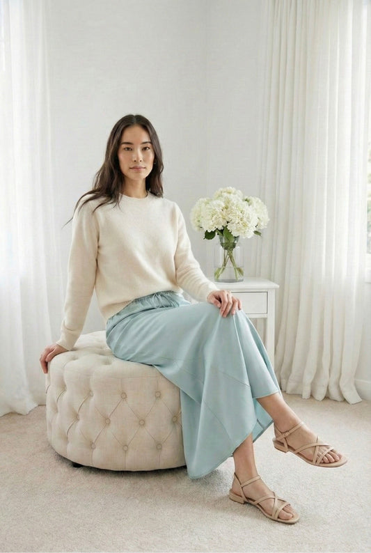 Model wearing Emory Park Tie Front Satin Midi Skirt in Light Green paired with cashmere sweater and sandals sitting on tufted ottoman in luxury apartment