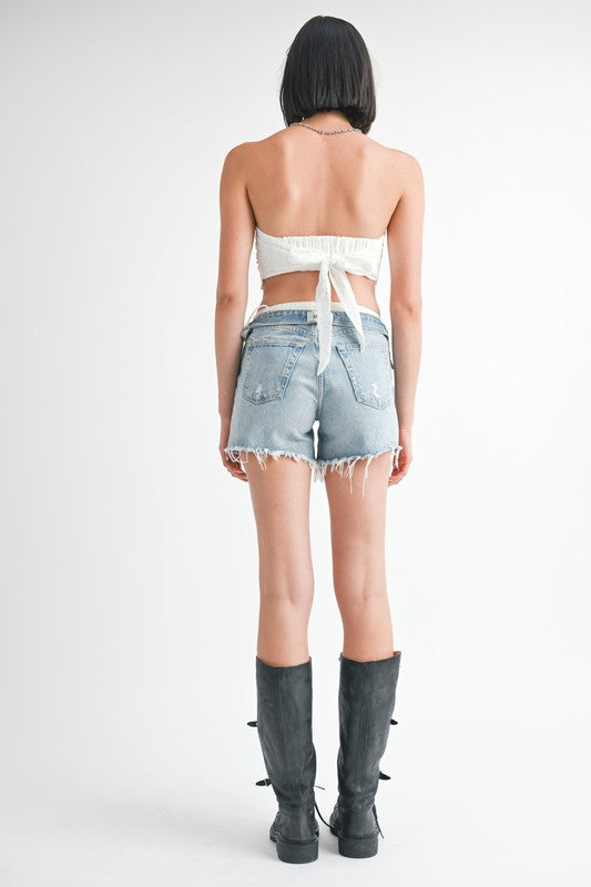 Back view of woman wearing Emory Park Cropped Eyelet Tube Top paired with denim shorts and black boots