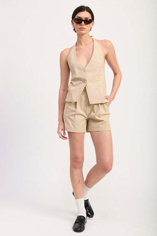 Model wearing Emory Park high waisted pleated shorts with matching sleeveless button vest and black shoes