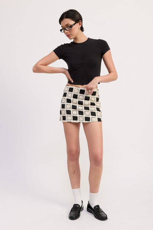 Woman wearing Emory Park Mini Jacquard Skirt with black and white checkered pattern paired with black top and loafers