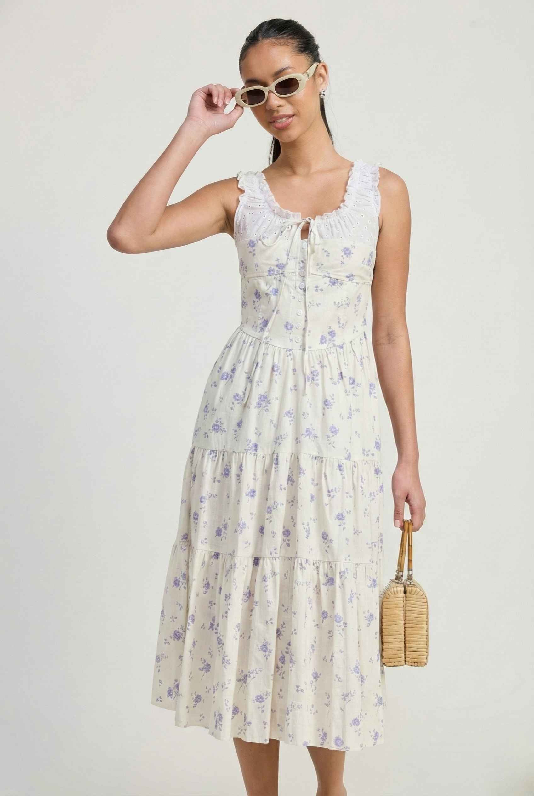 Woman wearing a Adeline Midi | Ivory Floral Eyelet Tiered Dress holding sunglasses against a plain background
