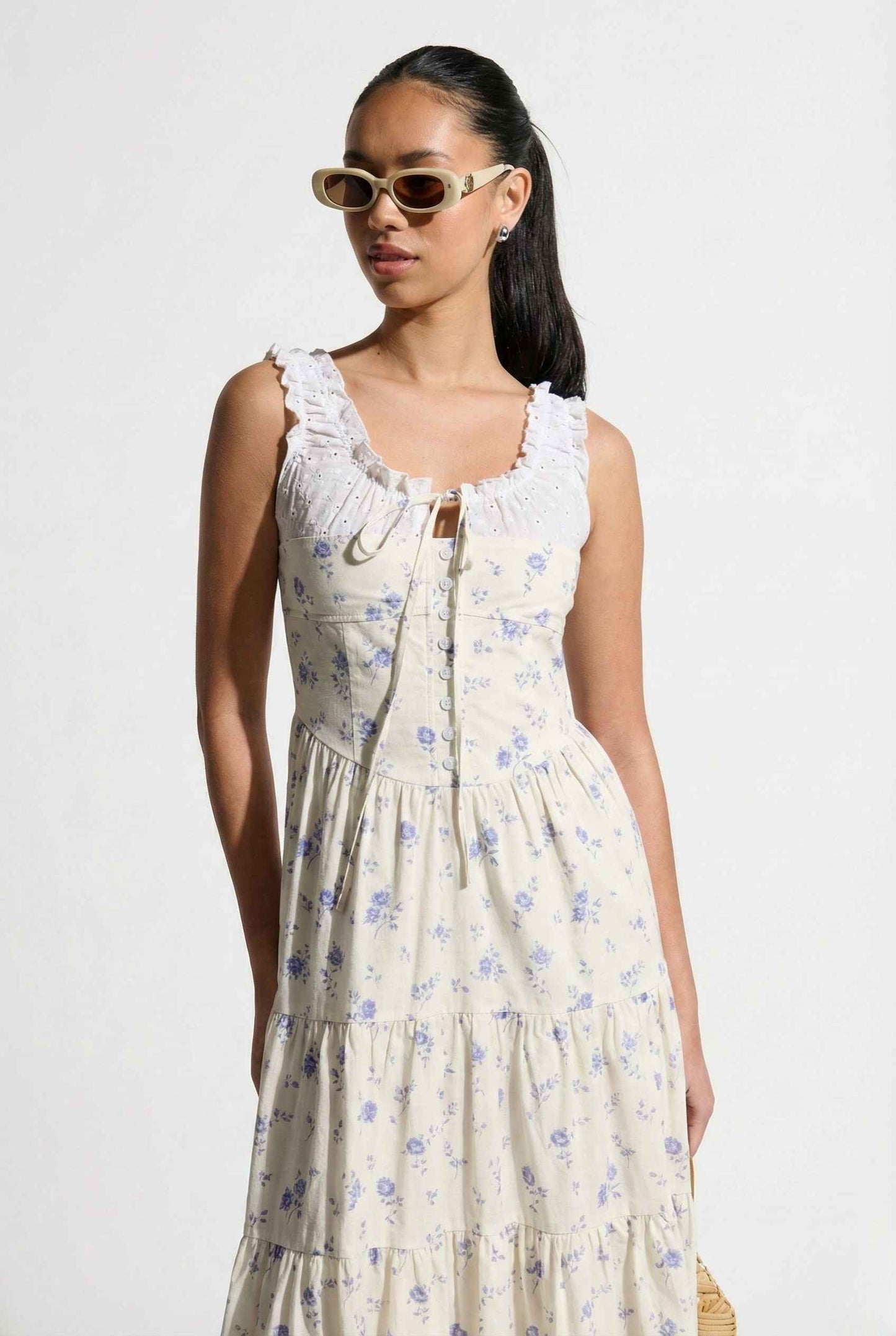 Woman wearing a Adeline Midi | Ivory Floral Eyelet Tiered Dress with sunglasses on a plain background