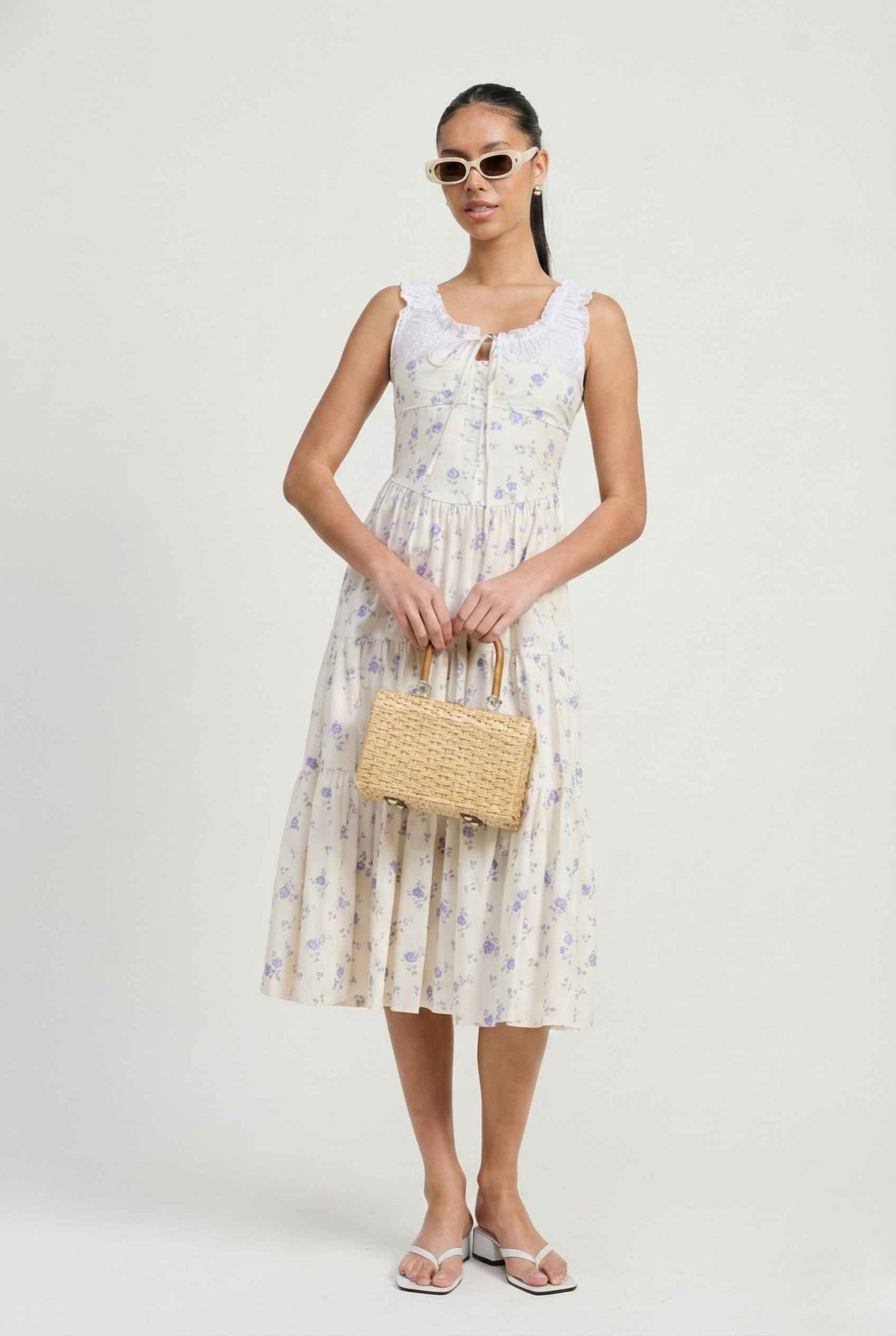 Woman holding a straw bag wearing a Adeline Midi | Ivory Floral Eyelet Tiered Dress on a background