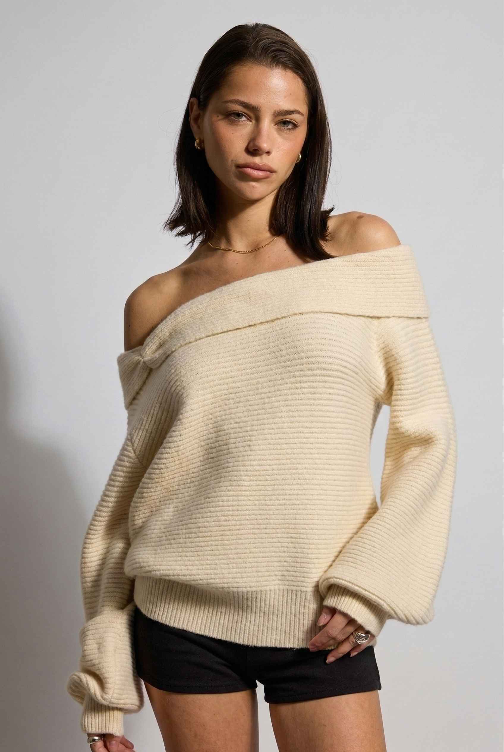 Model wearing Amara Top in Cream Ribbed Knit Twist-Front Off-Shoulder Sweater with micro shorts