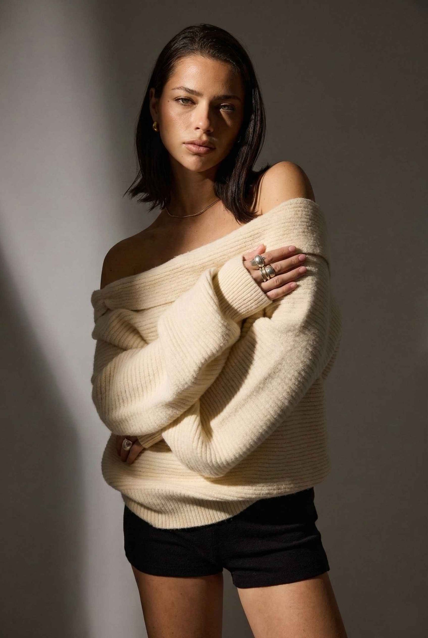 Model wearing Amara Top in Cream Ribbed Knit Twist-Front Off-Shoulder Sweater with micro shorts