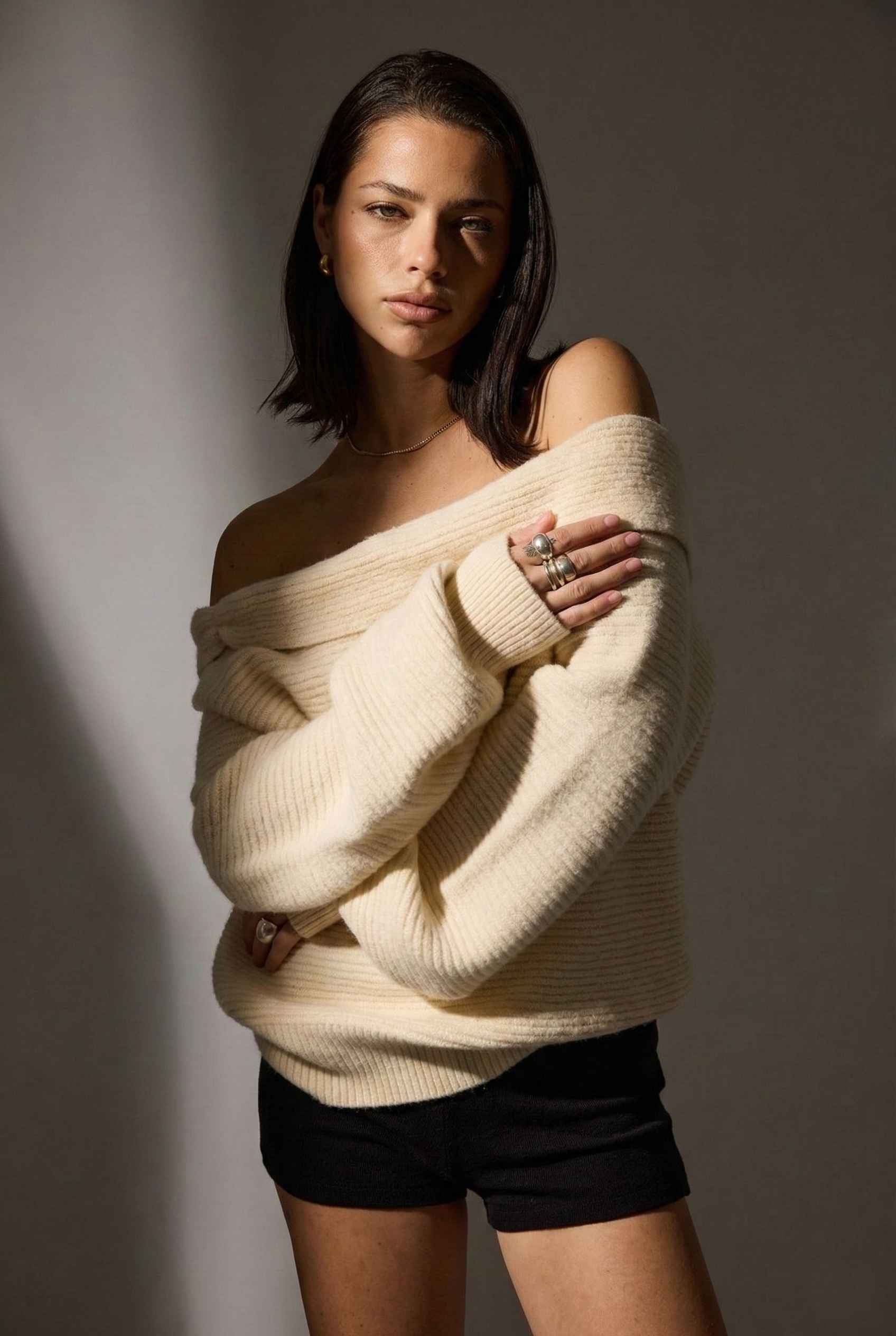 Model wearing Amara Top in Cream Ribbed Knit Twist-Front Off-Shoulder Sweater with micro shorts