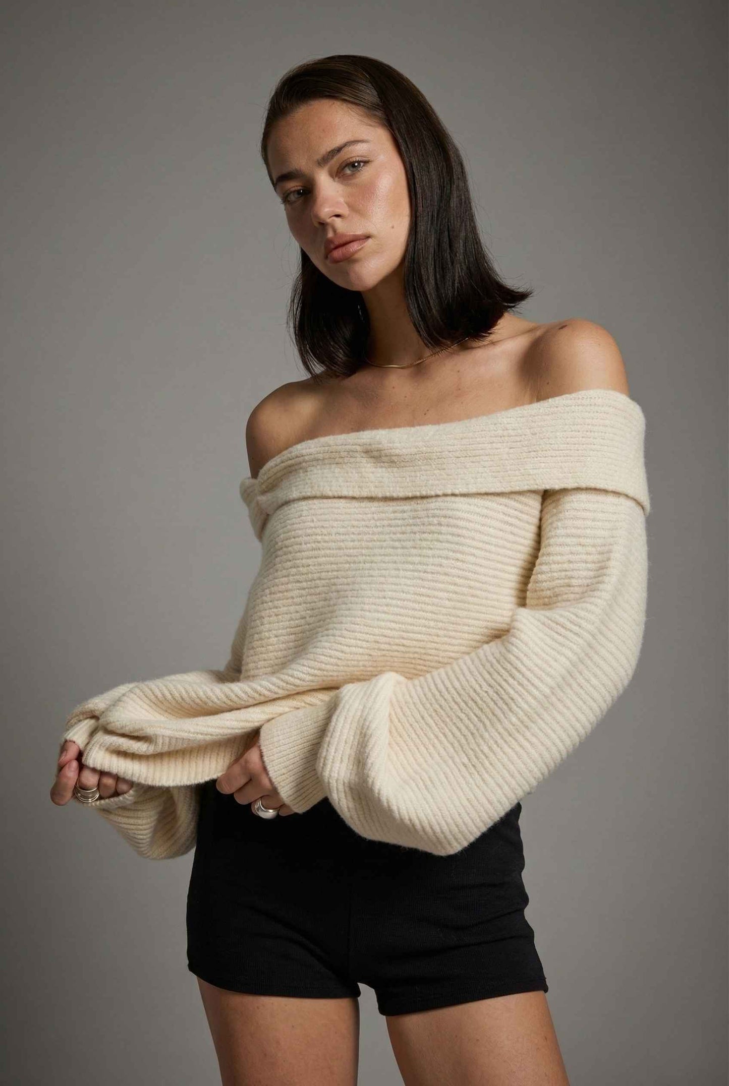 Model wearing Amara Top in Cream Ribbed Knit Twist-Front Off-Shoulder Sweater with micro shorts