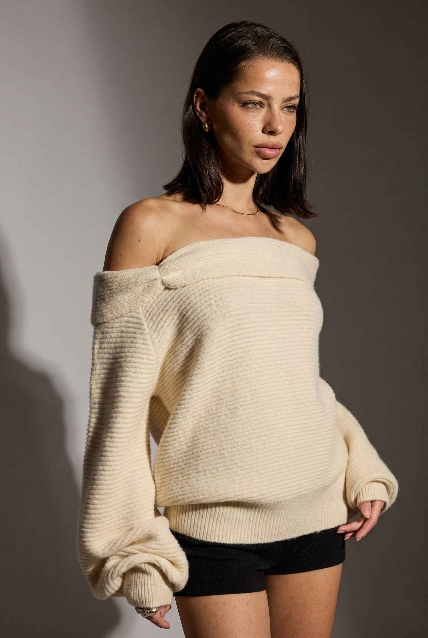 Model wearing Amara Top in Cream Ribbed Knit Twist-Front Off-Shoulder Sweater with micro shorts