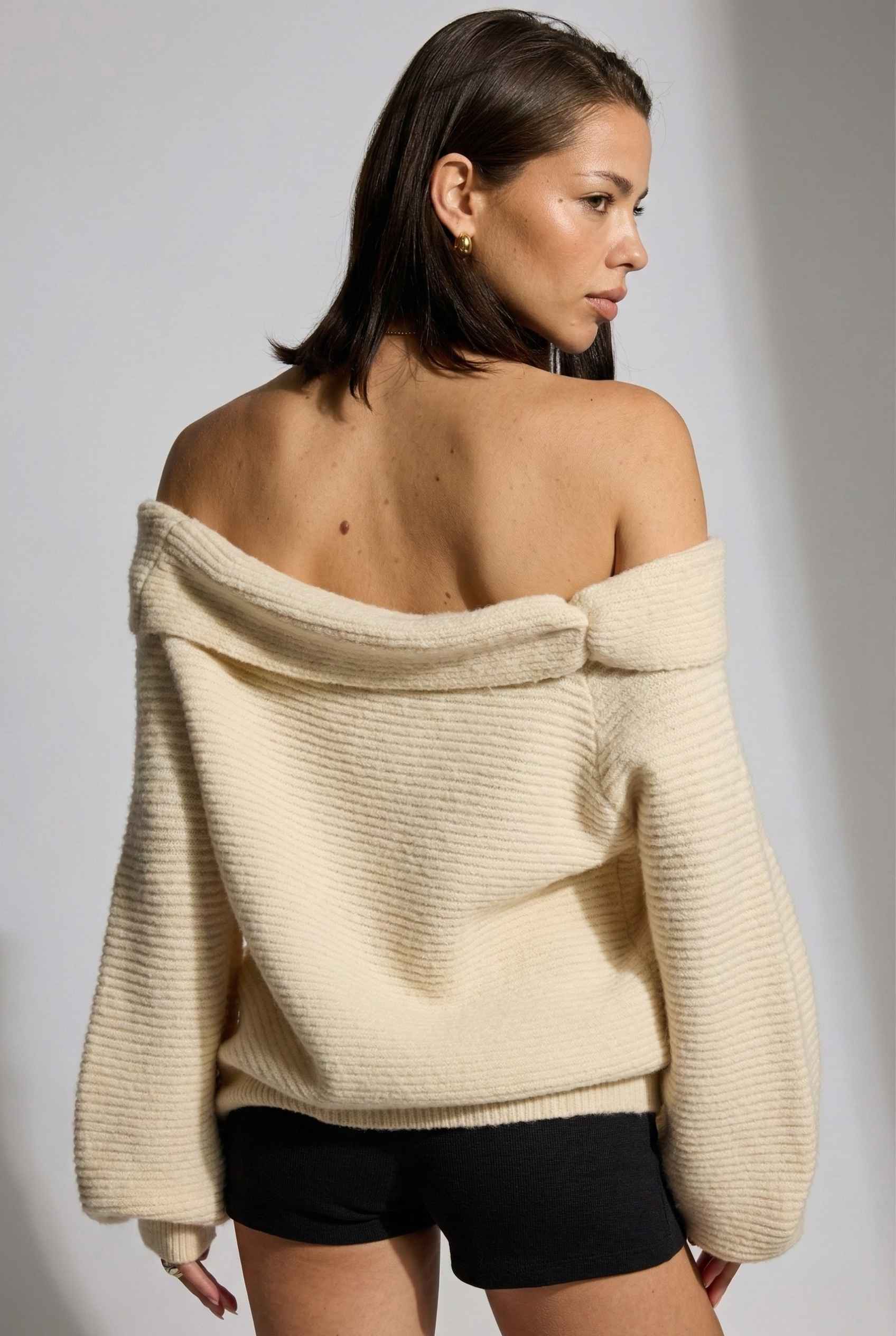 Model wearing Amara Top in Cream Ribbed Knit Twist-Front Off-Shoulder Sweater with micro shorts