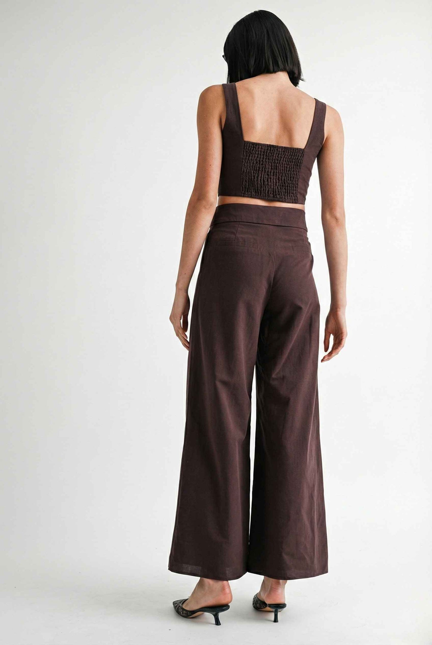 Woman wearing a Aria Top Chocolate Linen Blend Button Front Tie Crop Top and wide-leg pants on a background