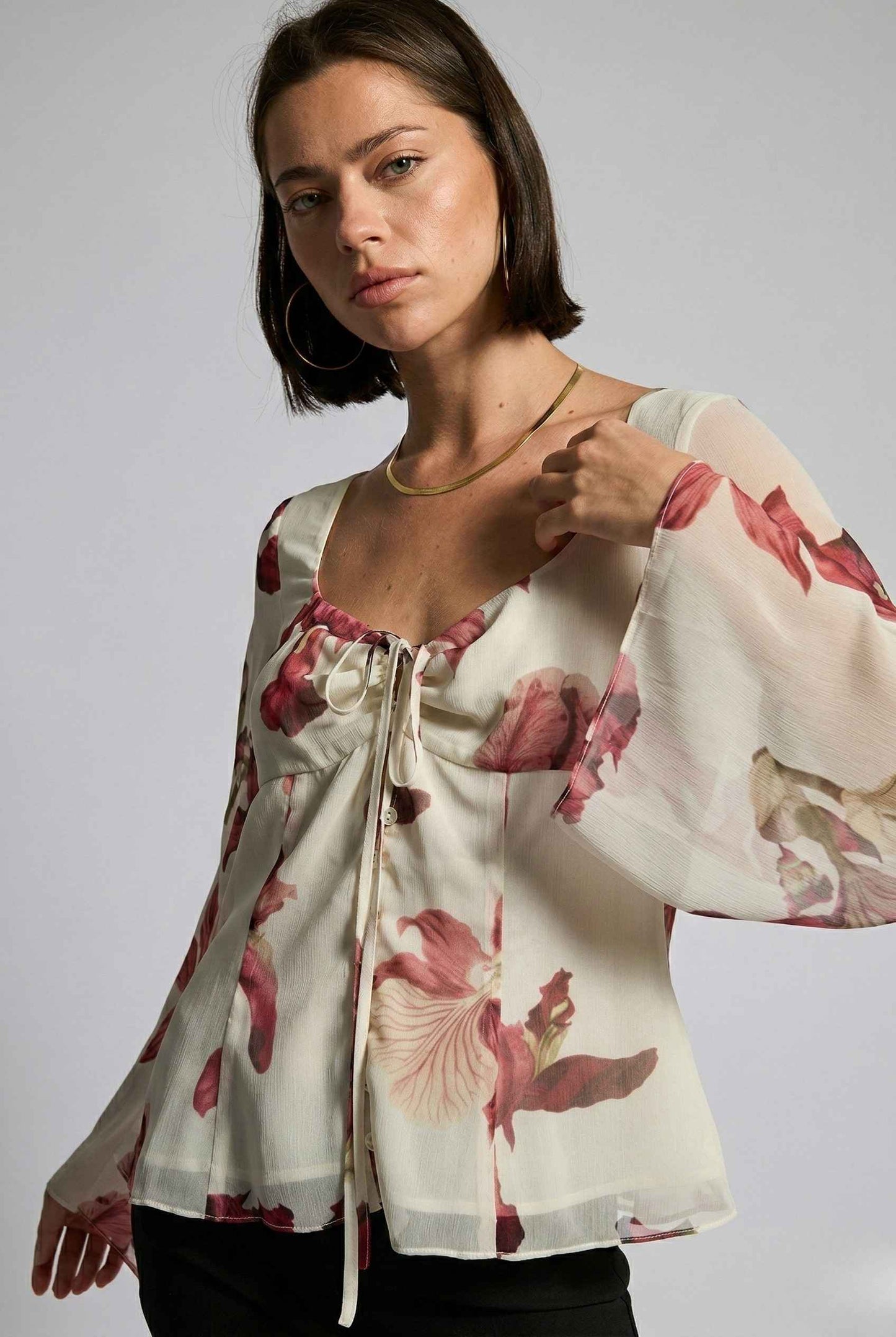 Woman wearing a Aria Top Ivory Floral Tie-Front Bell Sleeve Blouse with a plain background