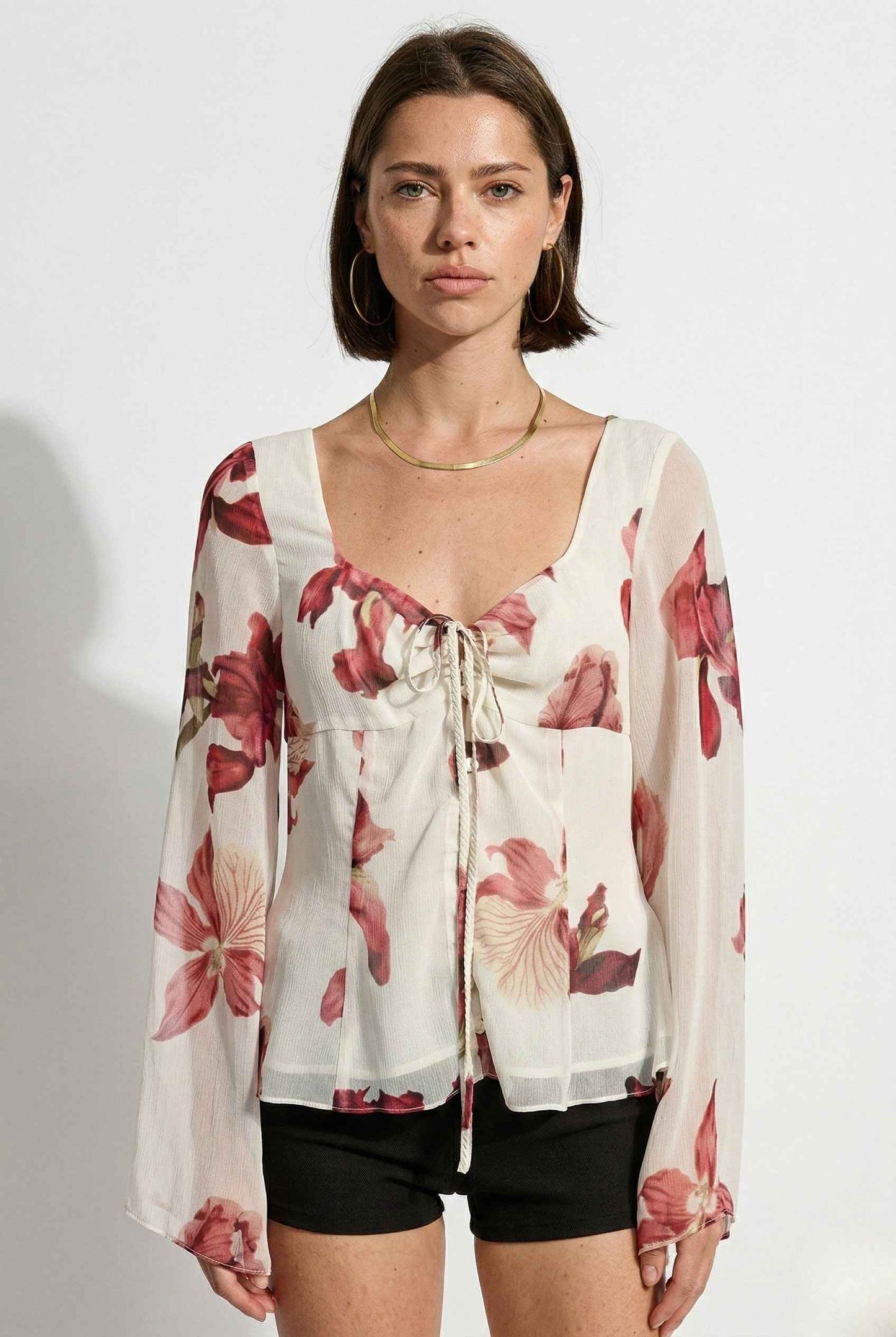 Woman wearing a Aria Top Ivory Floral Tie-Front Bell Sleeve Blouse with a plain background