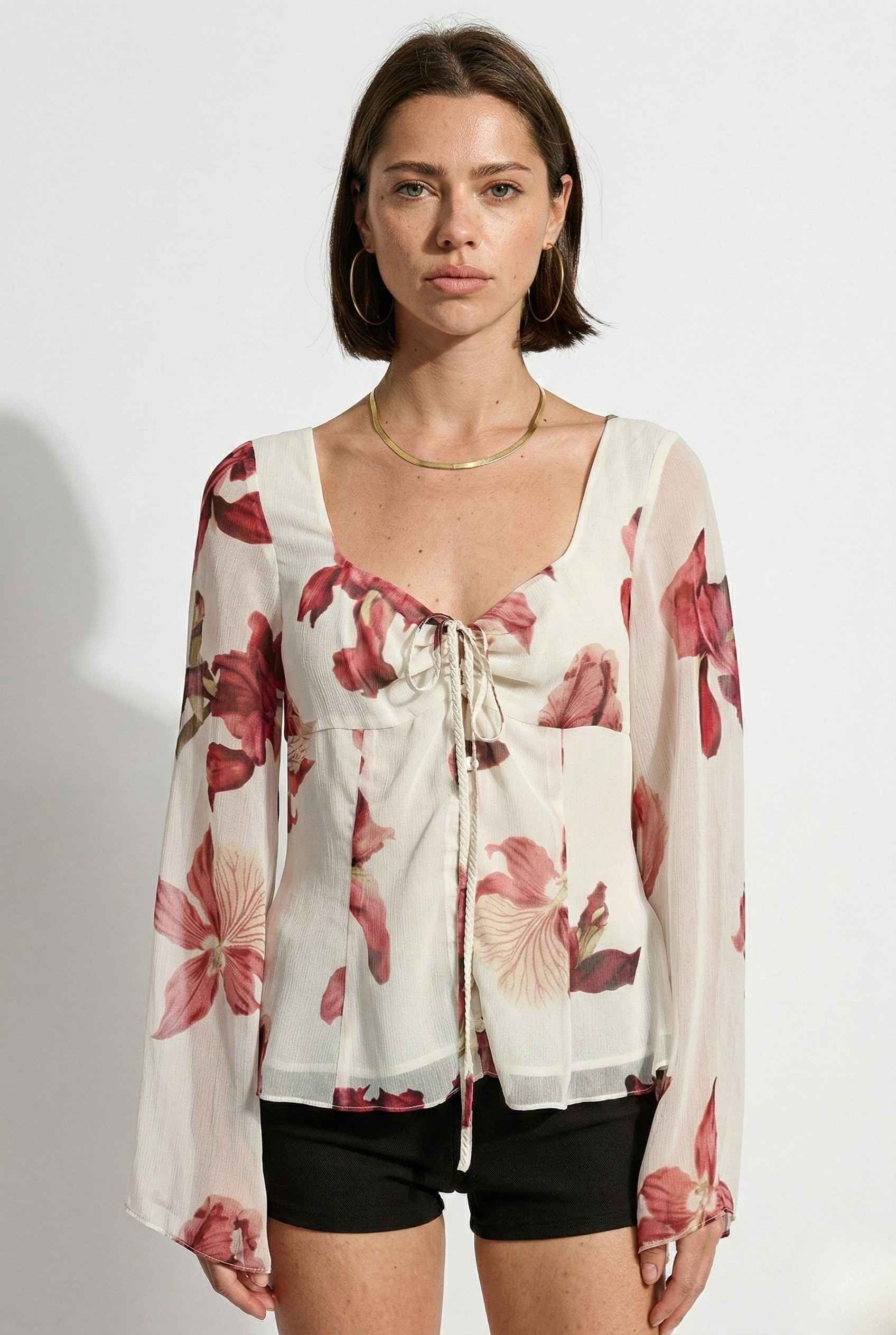 Woman wearing a Aria Top Ivory Floral Tie-Front Bell Sleeve Blouse with a plain background