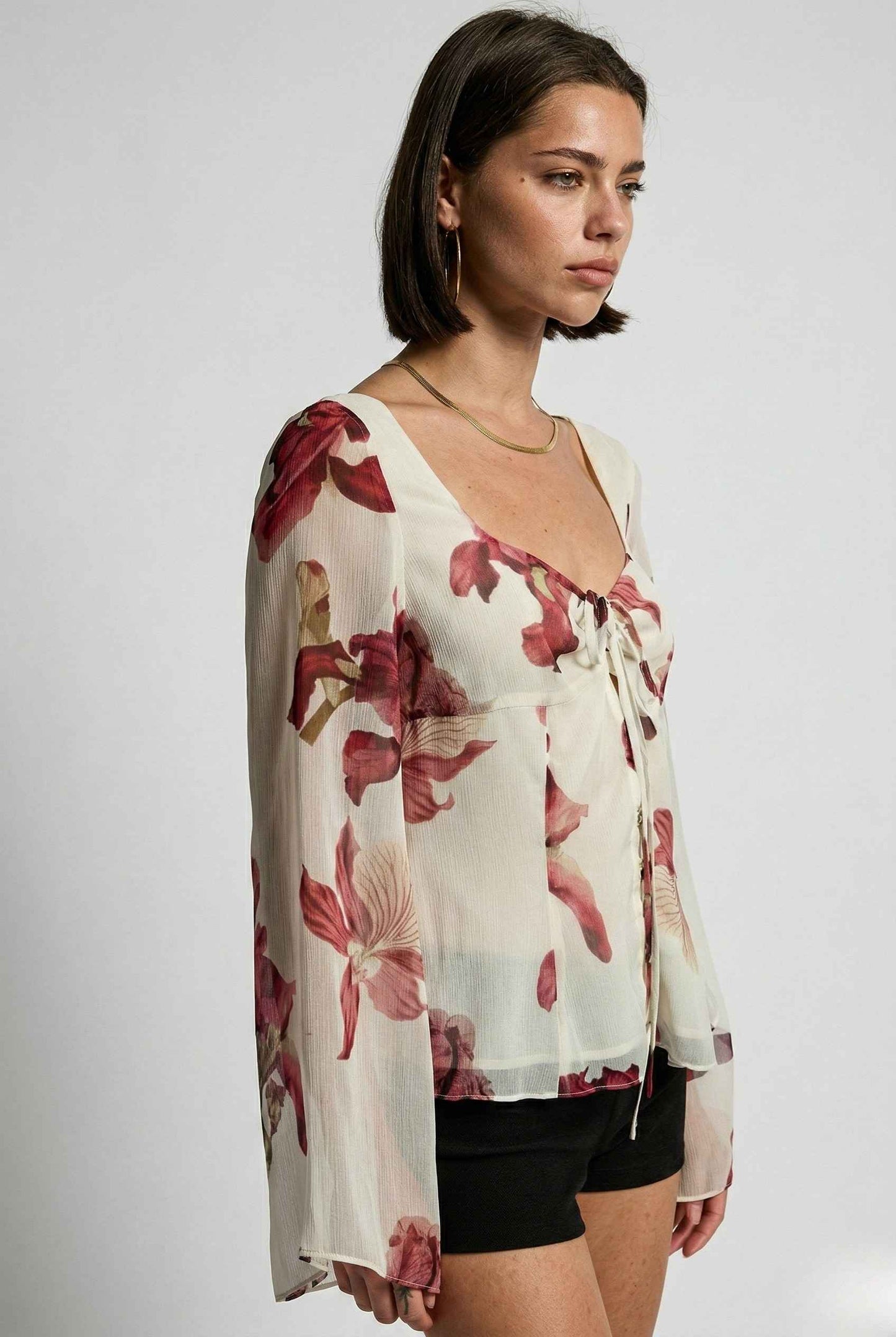 Woman wearing a Aria Top Ivory Floral Tie-Front Bell Sleeve Blouse with a plain background