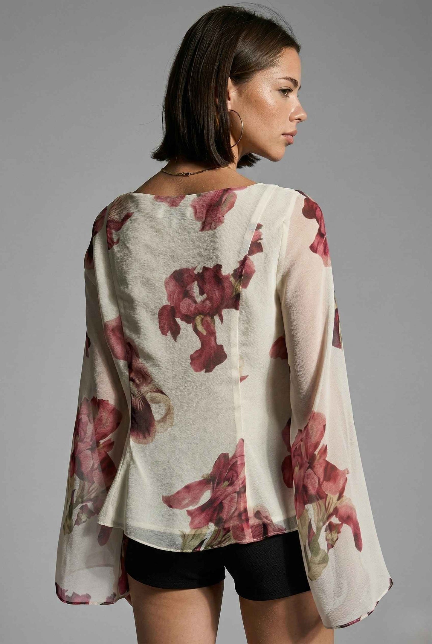 Woman wearing a Aria Top Ivory Floral Tie-Front Bell Sleeve Blouse with a gray background